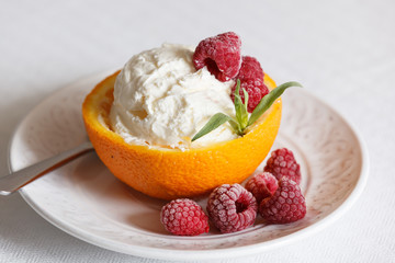 Closeup of a vanilla ice cream ball in an orange rug with raspberries on a white plate. Delicious sweet tropical dessert for the summer.