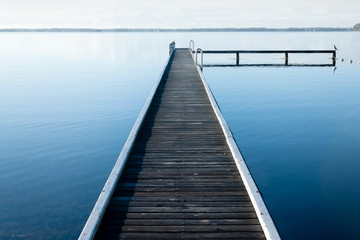 Obraz na płótnie Canvas Calm lake with wooden jetty and light fog on horizon
