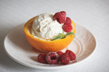 Closeup of a vanilla ice cream ball in an orange rug with raspberries on a white plate. Delicious sweet tropical dessert for the summer.