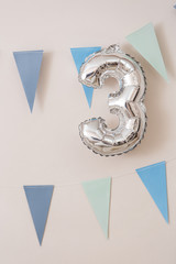 Big number 3 silver colors and blue paper garland flags on white wall background. Birthday decoration