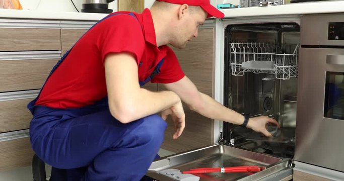 home appliance maintenance service - repairman working with dishwasher in domestic kitchen
