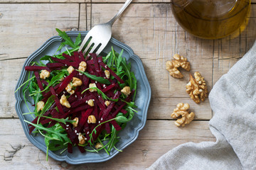 Vitamin salad of raw beets, arugula, walnuts and olive oil on a wooden table. Rustic style.