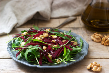 Vitamin salad of raw beets, arugula, walnuts and olive oil on a wooden table. Rustic style.