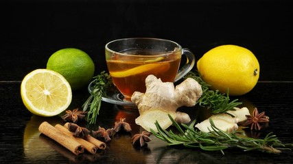 Spices for tea. A cup of tea, lemon, lime, ginger, anise stars, cinnamon sticks and a sprig of rosemary on a black background.