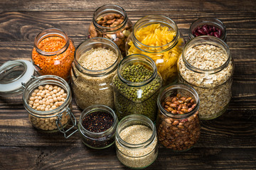 Cereals, Legumes, and beans in glass jars on wooden kitchen table. 