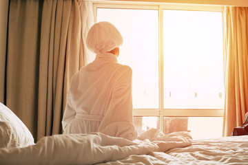 Beginning of a new day. Magnificent girl is sitting upstream the French window with beige blinds clothed in bath towel and bathrobe.