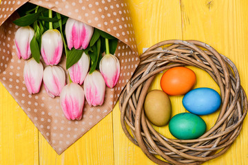 Obraz na płótnie Canvas Spring holiday. Happy easter season. Easter is coming. Collecting easter eggs. Spring vibes. Colorful eggs and bouquet fresh tulip flowers on yellow background top view. Tradition celebrate easter