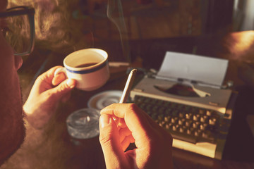 Young man writing on old typewriter while smoking cigar.