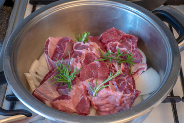 pieces of raw beef with onion and rosemary sprigs in metal bowl