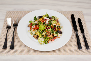 Eggplant salad with vegetables and walnuts and cutlery on a white plate.