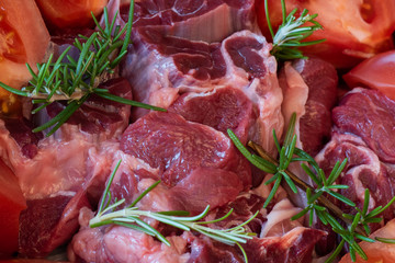 close-up of pieces of raw beef with tomatoes and sprigs of rosemary