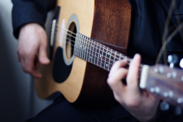 Fototapeta na wymiar A man in a black jacket plays a stylish wooden acoustic guitar with six strings