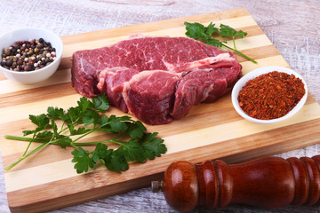 Raw beef steak with spices Leaves of coriander on wooden cutting board. Ready for cooking.