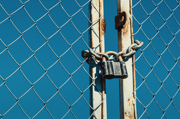 Padlock with chain on a metal gate with a metal grill. Against the blue sky