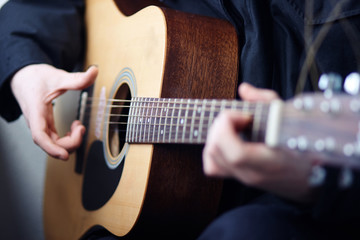 Fototapeta premium A man in dark clothes playing acoustic wooden six-string guitar beautiful melodies and songs