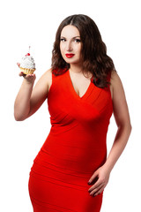 A woman in a red dress holding a cake with cream and a cherry. The girl looks at the sweetness and wants to eat it. Isolated portrait on white background