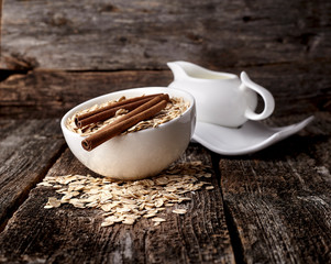 Oatmeal or oat flakes with milk and cinnamon on dark wooden table