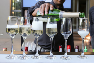 barman pouring champaign in six glasses with blue berries