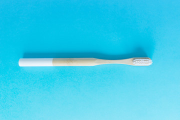 ecology natural bamboo toothbrush with wooden handle and white bristles on blue background under natural light