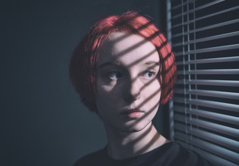 young redhead girl sad at night near window with blinds