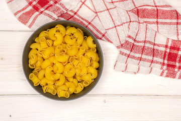 Lot of whole raw pasta pipe rigate variety in a grey ceramic bowl flatlay on white wood
