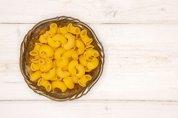 Lot of whole raw pasta pipe rigate variety in old iron bowl flatlay on white wood