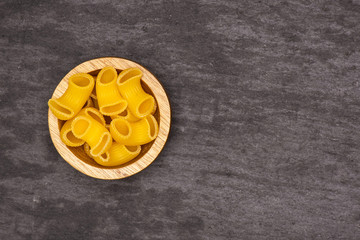 Lot of whole raw pasta pipe rigate variety with wooden bowl flatlay on grey stone