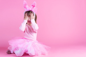 Cute pink young girl child daughter wears pink dress like rabbit playing in easter holiday game with rabbit ears on isolated pink background. Spring is coming and Easter holiday concept