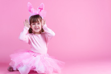 Obraz na płótnie Canvas Cute pink young girl child daughter wears pink dress like rabbit playing in easter holiday game with rabbit ears on isolated pink background. Spring is coming and Easter holiday concept