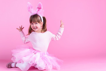 Obraz na płótnie Canvas Cute pink young girl child daughter wears pink dress like rabbit playing in easter holiday game with rabbit ears on isolated pink background. Spring is coming and Easter holiday concept