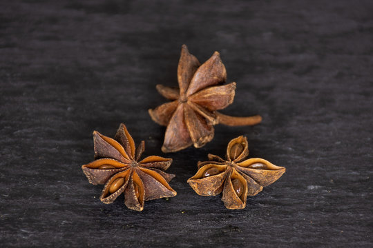 Group of three whole dry brown star anise fruit on grey stone