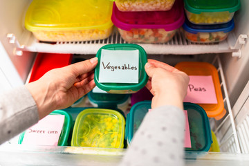 Woman placing container with frozen vegetables in freezer.