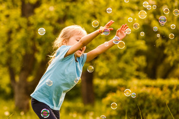 Funny little girl catching soap bubbles in the summer on nature. Background toning instagram filter. Happy childhood concept