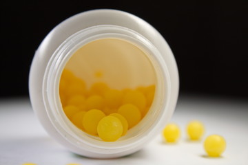 Soft focus close up of a white bottle with yellow pills laying on its side with black background