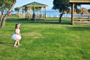 Cute toddler girl having fun in park in tropical resort near the seashore on back view. Summer holiday concept.