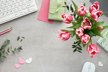 Springtime flat lay with keyboard, mouse, cards, bunch of pink tulips, eucalyptus and gift boxes