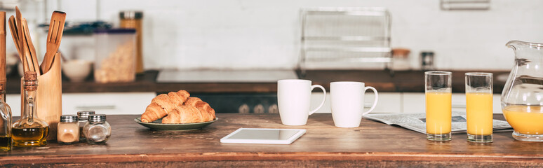 cups near glasses with orange juice and digital tablet in kitchen