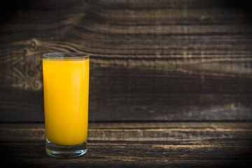 Glass of fresh tropical juice with yellow fruit on wooden table