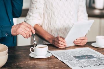 cropped view of man holding spoon near cup with coffee near wife holding digital tablet