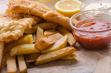 Traditional British street food fish and chips with ketchup and tartar sauces on parchment paper