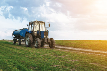 Tractor with a barrel trailer rides on a green field