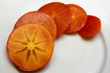 fresh, ripe, juicy persimmon sliced ​​in round slices on a white plate
