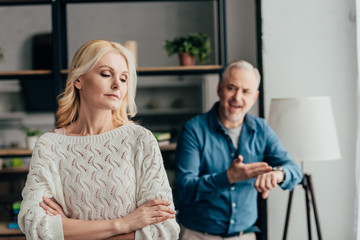 Obraz premium selective focus of woman standing with crossed arms while husband arguing on background