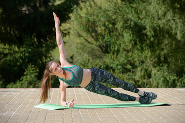 Image of young caucasian sporty woman in tracksuit doing side plank while training in green park