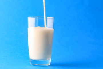 Pouring milk into glass on blue background