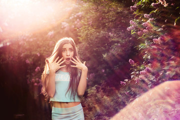 Wonderful spring. A beautiful young girl enjoys nature and sunlight among the blossoming lilac.