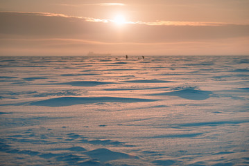 Frozen sea. Sunrise. Two fishermen and a ship in the background