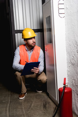 Handsome fireman looking at fire panel while sitting and holding clipboard