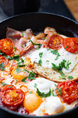 Fried eggs with bacon, toast and tomatoes in a pan