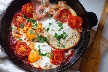 Fried eggs with bacon, toast and tomatoes in a pan